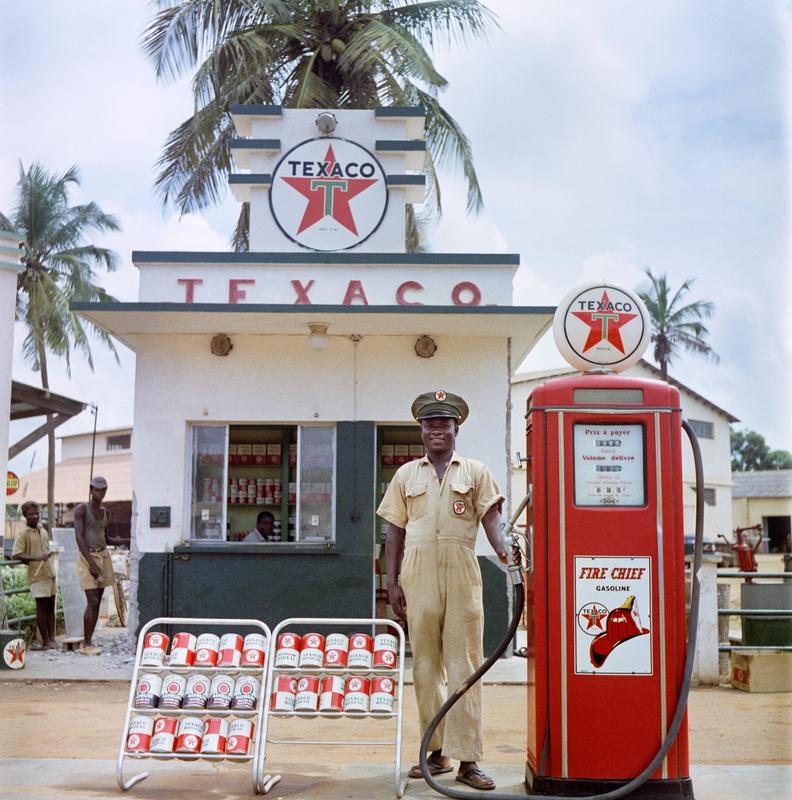 Color image of a man in a uniform standing outside of a Texaco gas station